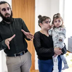 Man med skägg och glasögon gestikulerar. Bredvid honom håller en kvinna, som liknar Muhammeds hustru, ett litet barn.