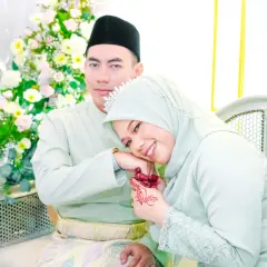 Ett lyckligt brudpar, klädda i ljusgrönt, omgivna av blommor. Hon vilar huvudet mot hans arm, en vacker dua for marriage.