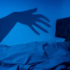 En skugga av en hand sträcker sig mot en sovande person i mörkret, en bild som kan påminna om upplevelser av sleep paralysis inom islam.
