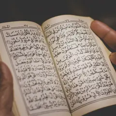 Händer håller en öppen Koran, där kraftfulla Koranverser läses.