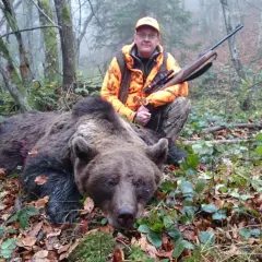 Jägare med gevär poserar bredvid en död björn i skogen. En påminnelse om att inte samla rikedomar, som i surah takasur.