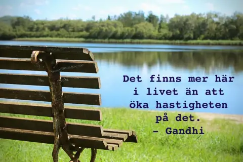 En bänk vid en sjö med texten "Det finns mer här i livet än att öka hastigheten på det. - Gandhi". En påminnelse om att njuta av lugnet, som en دعاء يوم السبت.