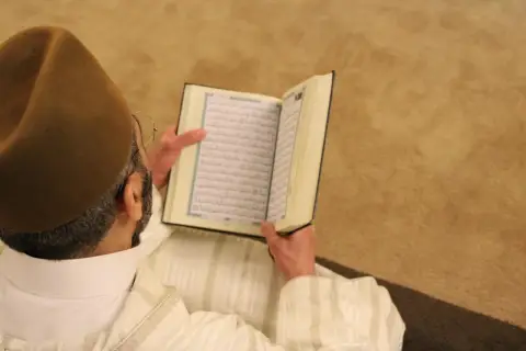 Man i brun hatt läser Koranen. Fajr-bönen består av två rakat.