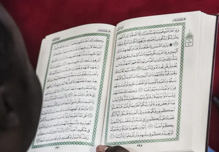 En person läser Koranen, en helig bok inom islam. Texten på sidan kan tolkas som en del av sharia lagar.