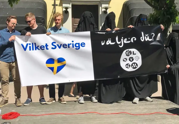 Människor håller en banderoll med texten "Vilket Sverige" och en svensk hjärta, samt "Väljer du?". Debatten om böneutrop i Sverige fortsätter.