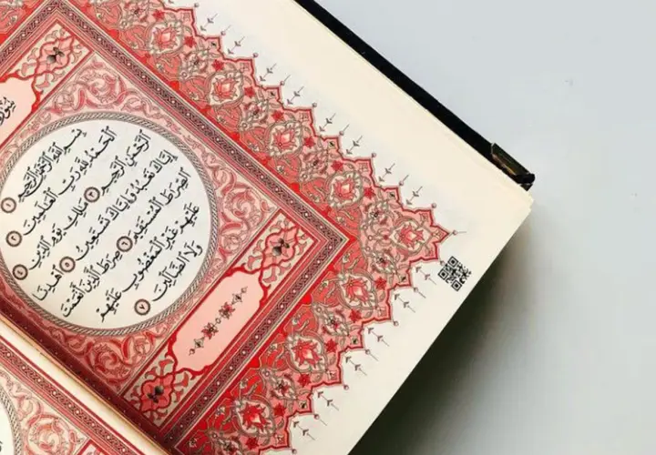 En öppen Koran med vackra röda mönster. Sura Al-Fatiha, den första suran i Koranen, visas.