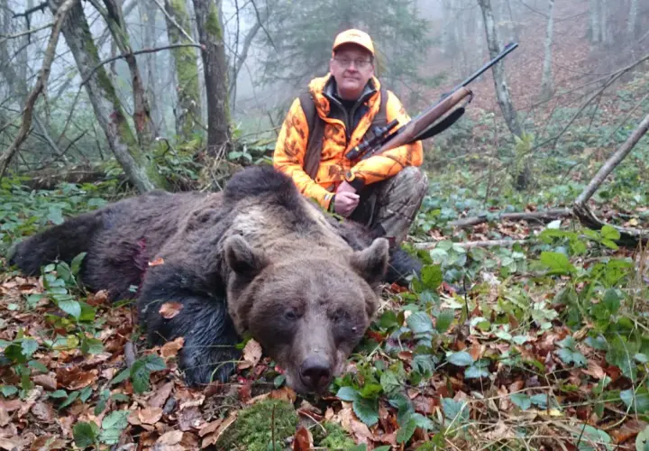 Jägare med gevär poserar bredvid en död björn i skogen. En påminnelse om att inte samla rikedomar, som i surah takasur.