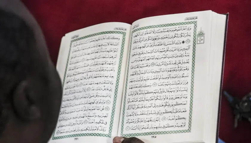 En person läser Koranen, en helig bok inom islam. Texten på sidan kan tolkas som en del av sharia lagar.