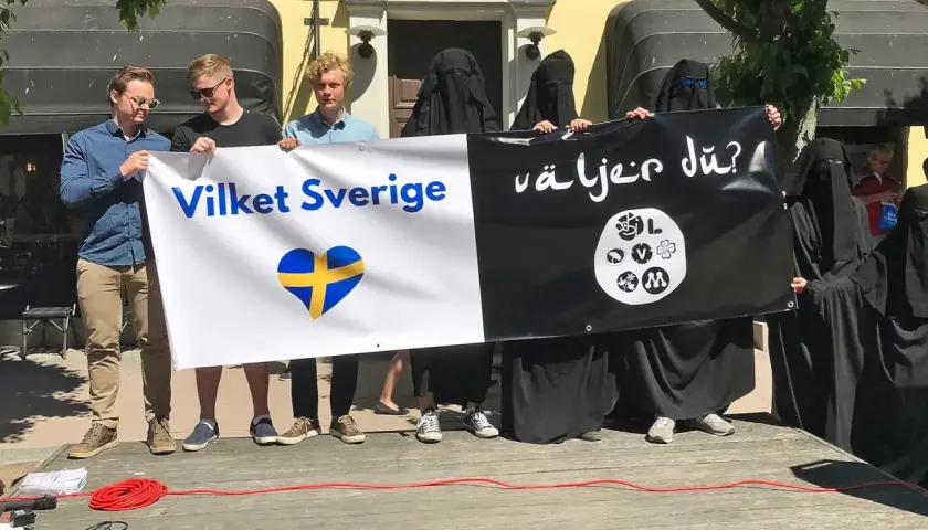 Människor håller en banderoll med texten "Vilket Sverige" och en svensk hjärta, samt "Väljer du?". Debatten om böneutrop i Sverige fortsätter.