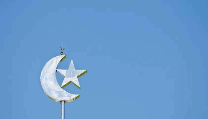 En glänsande halvmåne med en stjärna, en symbol för islam, mot en klarblå himmel.