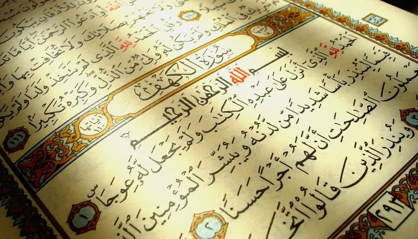 En öppen Koran med texten Surah Al-Kahf. Ljuset faller över sidorna med arabisk skrift.