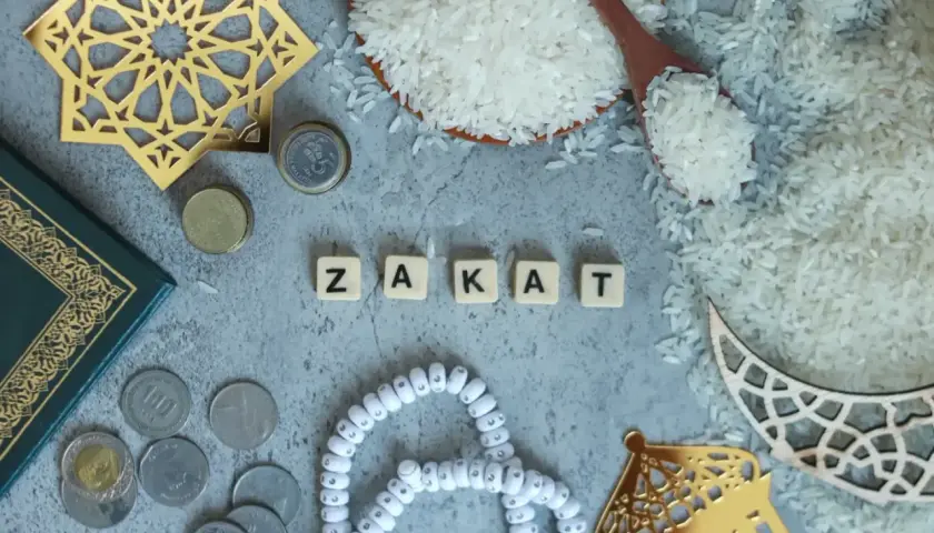 Rismängd, mynt och en bok bredvid bokstäverna som bildar ordet "Zakat", en viktig del av islamisk välgörenhet.