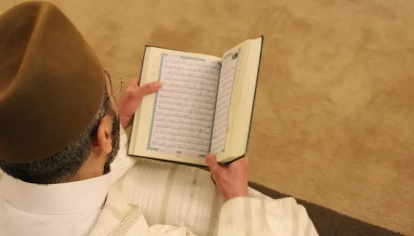 Man i brun hatt läser Koranen. Fajr-bönen består av två rakat.