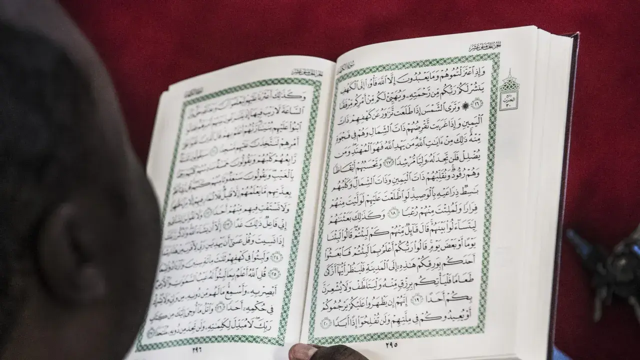 En person läser Koranen, en helig bok inom islam. Texten på sidan kan tolkas som en del av sharia lagar.