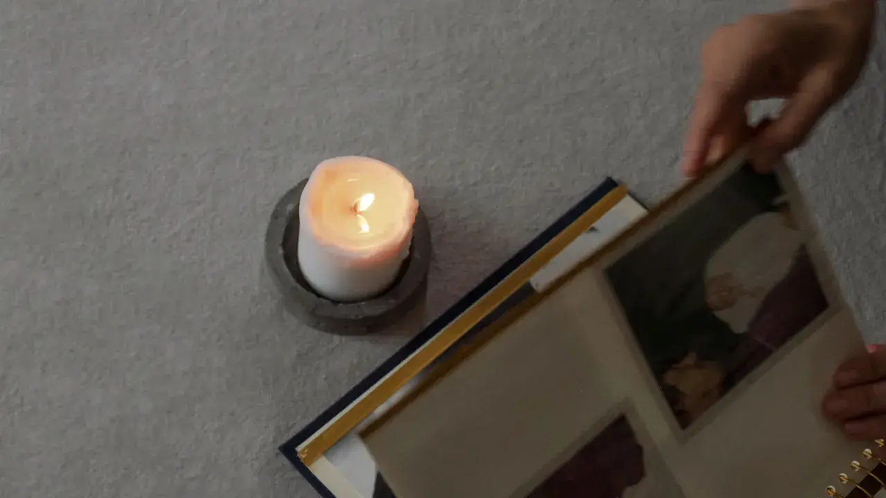 Ett tänt ljus och en fotoalbum. En hand bläddrar i albumet, kanske för att minnas någon. En dua när någon dör.