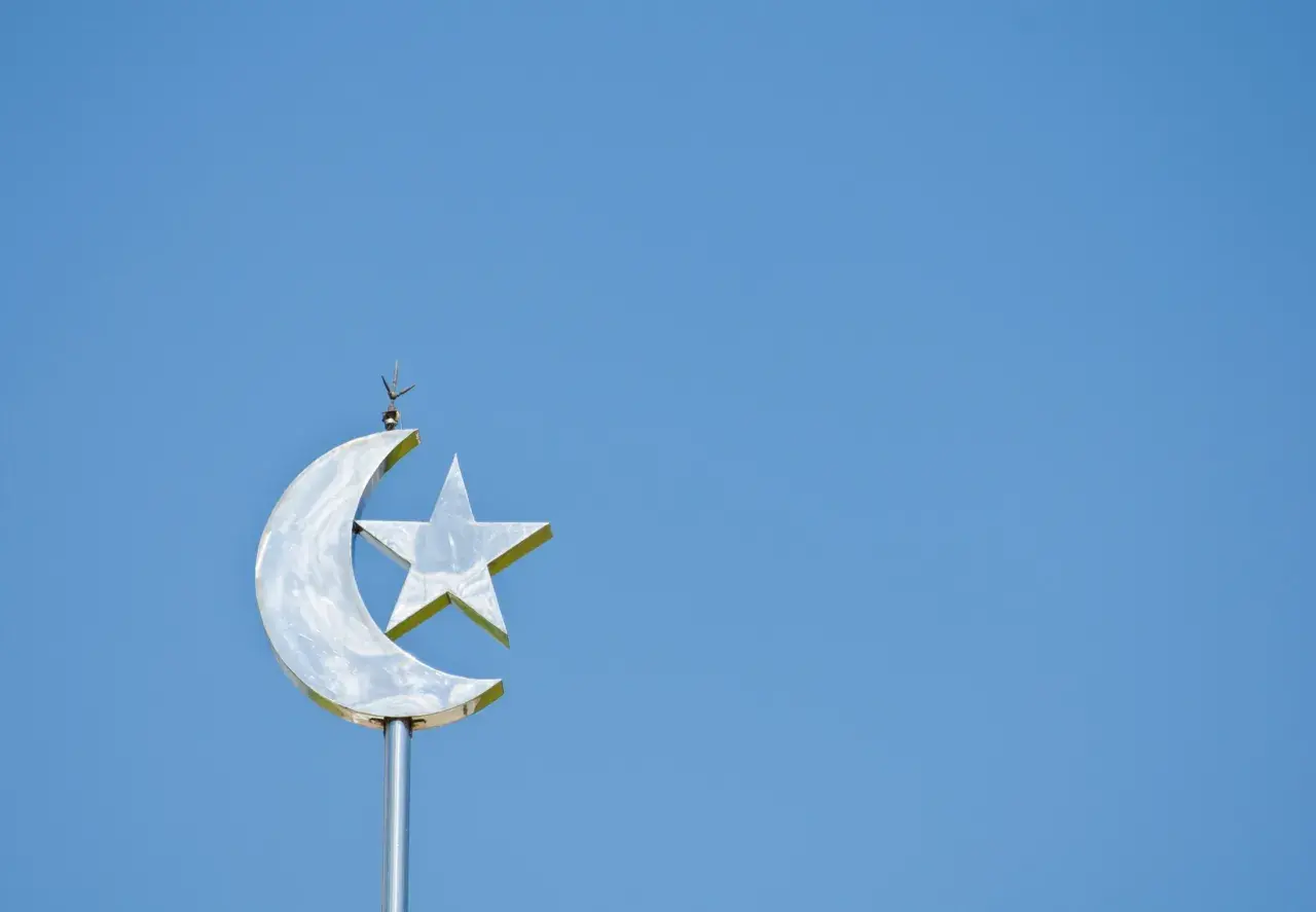 En glänsande halvmåne med en stjärna, en symbol för islam, mot en klarblå himmel.