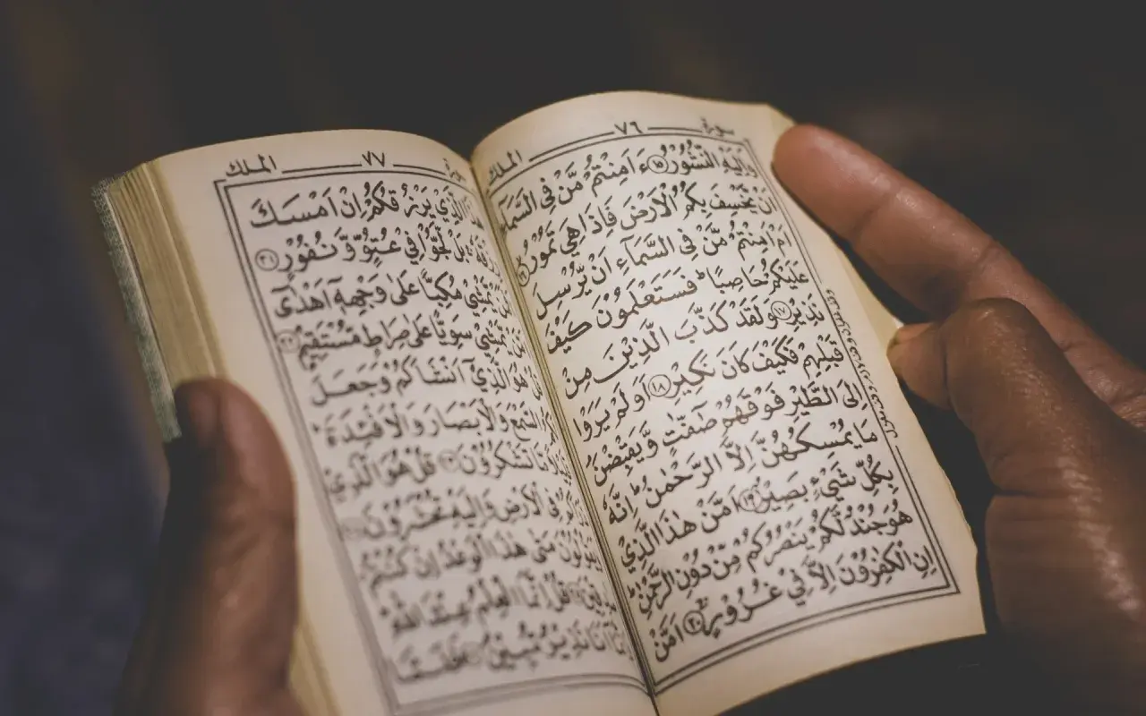 Händer håller en öppen Koran, där kraftfulla Koranverser läses.