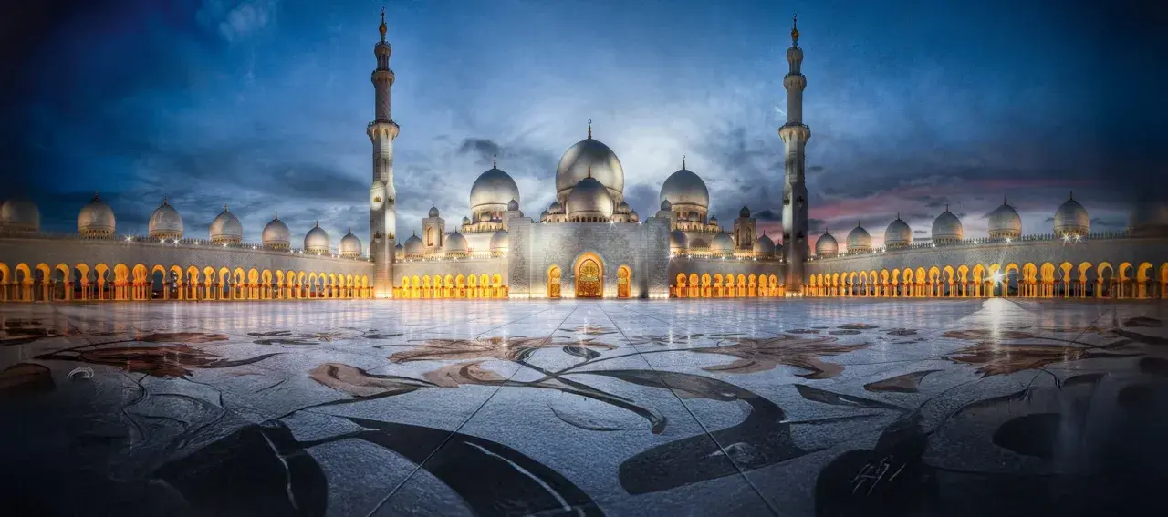 En storslagen moské upplyst i skymningen, med sina kupoler och minareter som speglar sig i den blöta marken. En påminnelse om islams fem pelare.