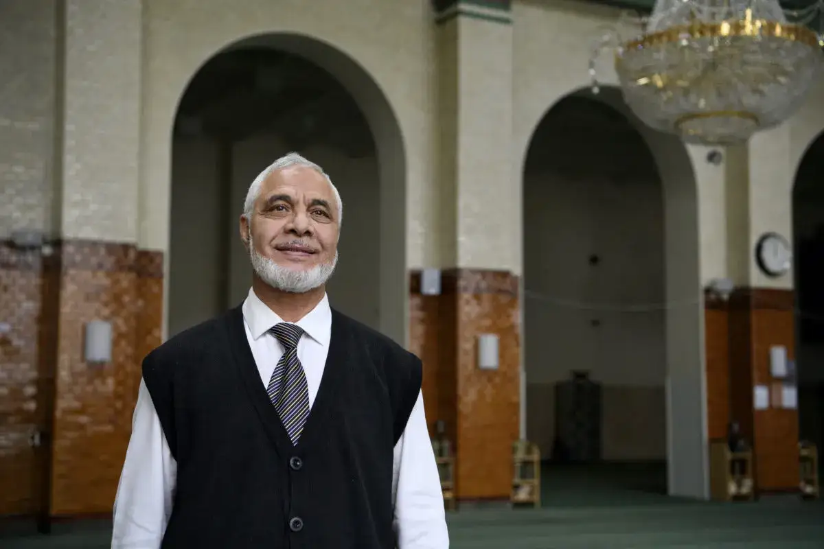 En leende muslimsk domare med grått skägg står i en moské.