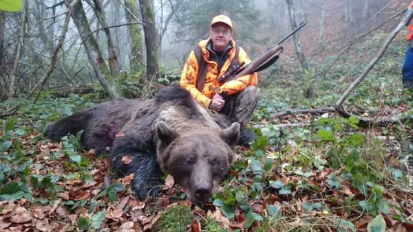 Jägare med gevär poserar bredvid en död björn i skogen. En påminnelse om att inte samla rikedomar, som i surah takasur.